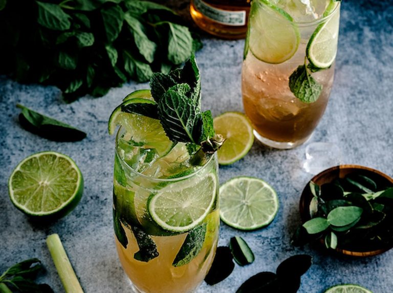 A cocktail of spiced rum garnished with limes and mint